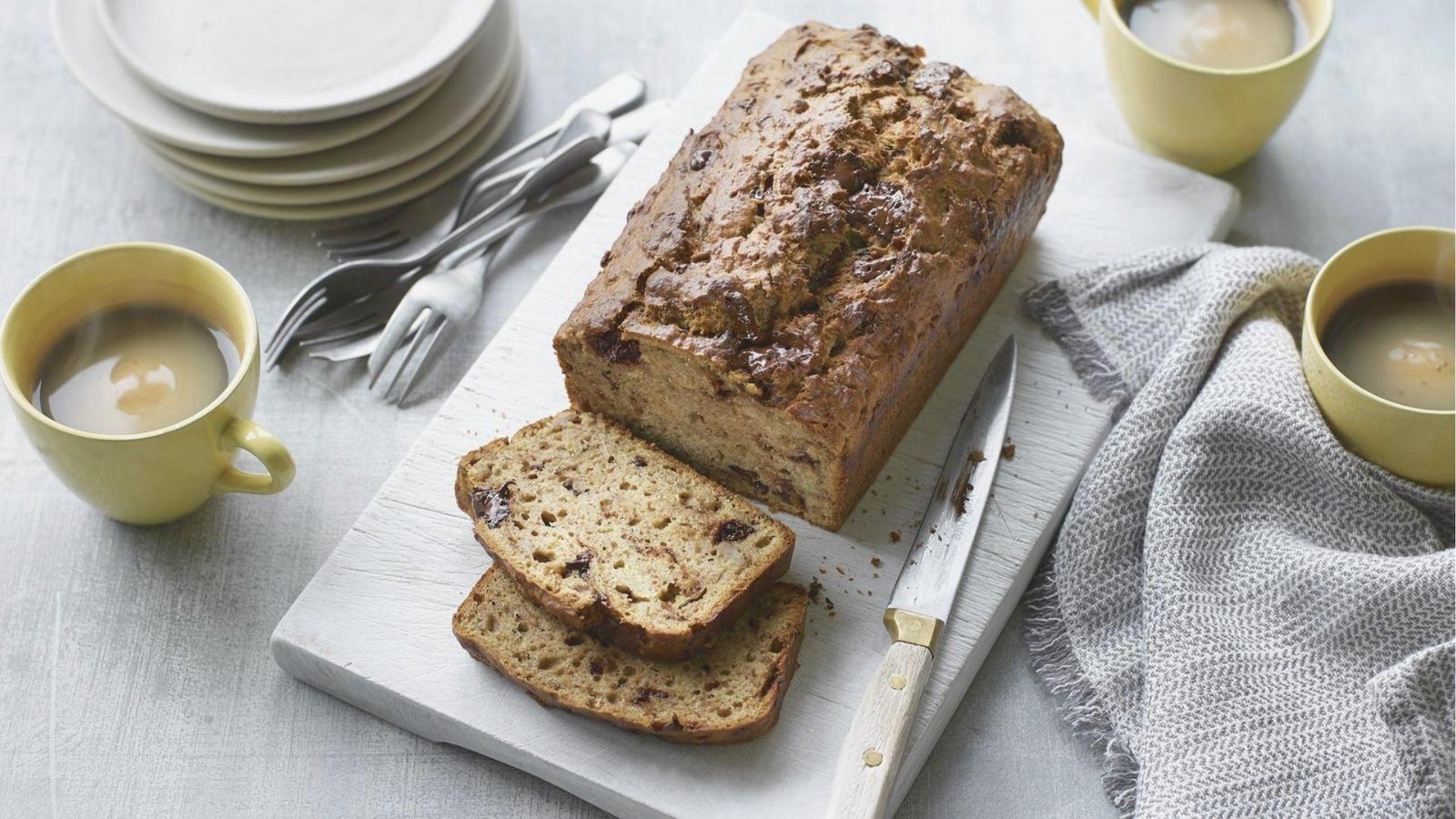 Sliced coffee chocolate chip bread on a white board with two steaming cups of coffee.