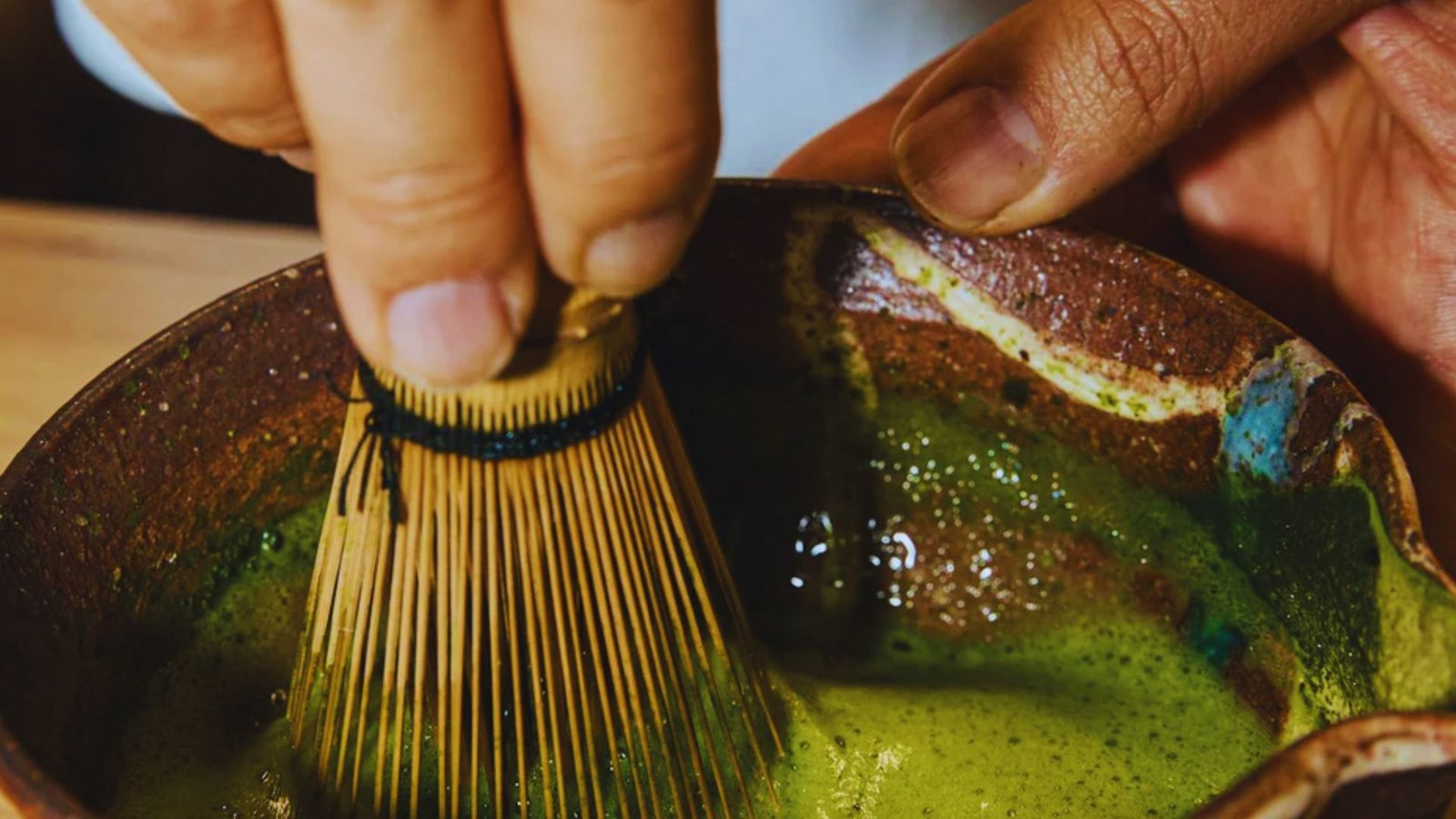 Whisking matcha powder with hot water to create a smooth matcha base