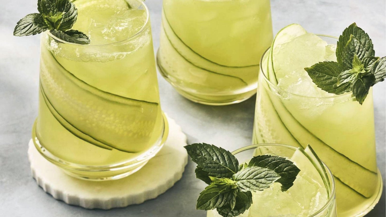 Four chilled glasses of cucumber mint agua fresca with long cucumber ribbons, ice, and mint sprigs
