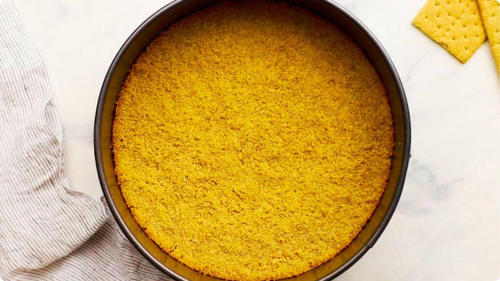 An overhead shot shows a 6-inch springform pan lined with an even layer of golden graham cracker crust.