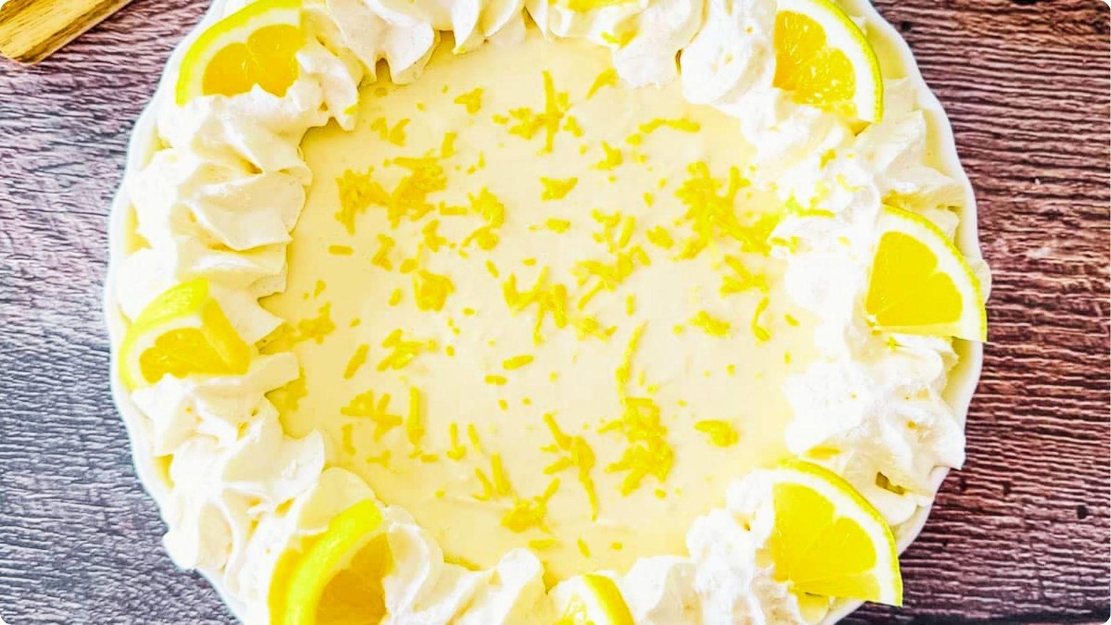Top-down view of a sour cream lemon pie garnished with piped whipped cream border and lemon wedges.