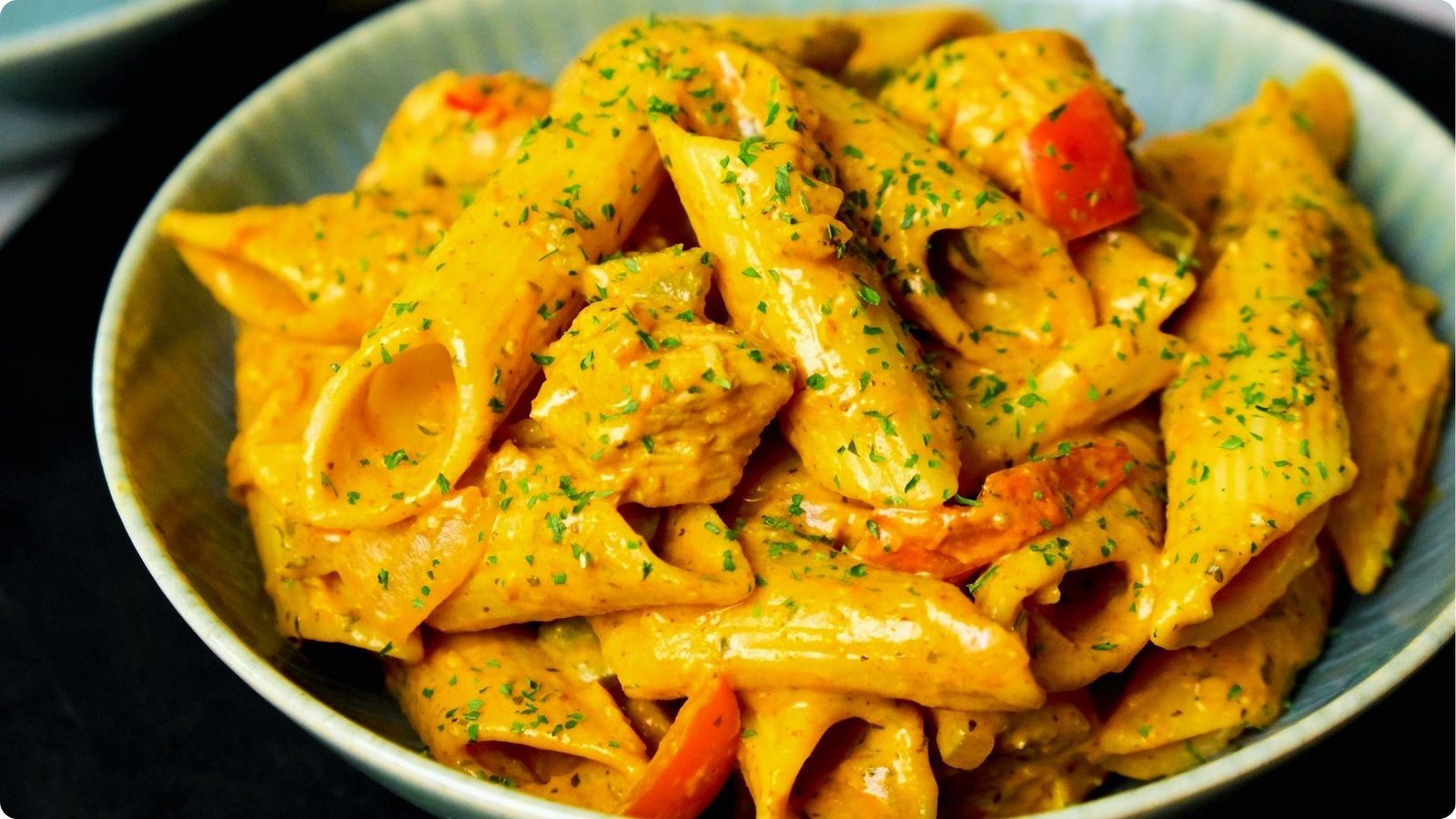 Close-up of creamy chipotle chicken penne pasta in a blue ceramic bowl.