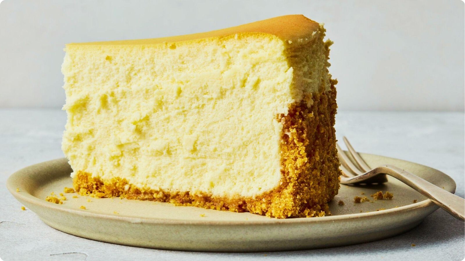 A thick slice of 6-inch cheesecake on a ceramic plate shows dense, creamy vanilla filling and a golden brown top.