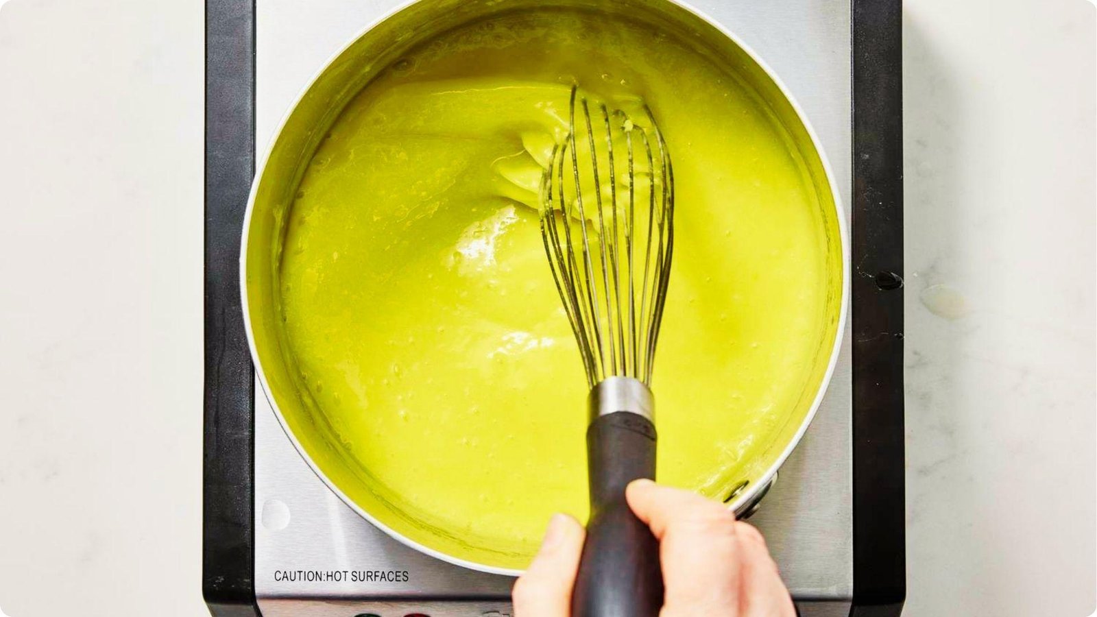 Top-down shot of bright yellow lemon pie filling being whisked in a saucepan.