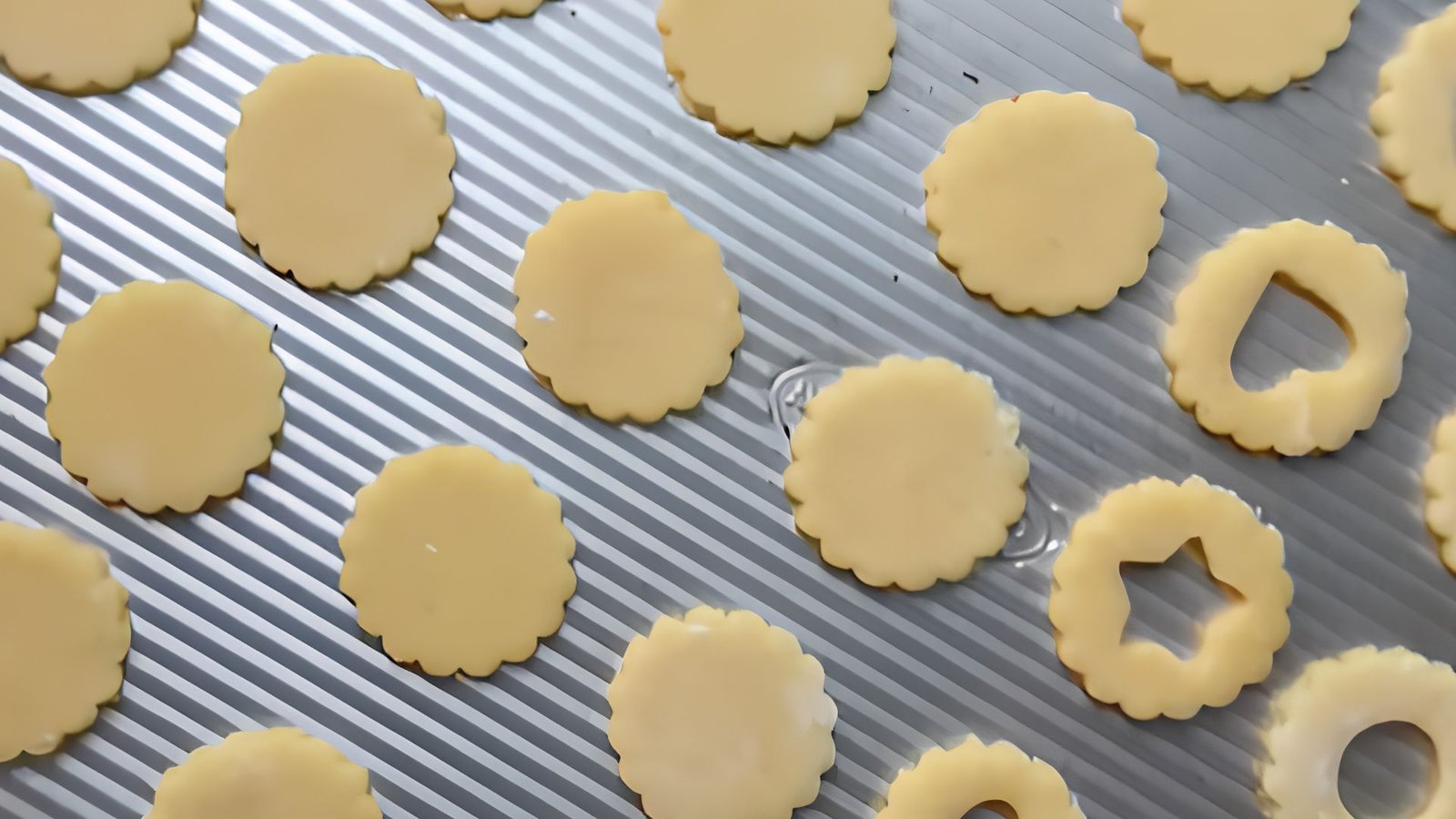 Freshly baked Linzer cookies cooling on a baking tray, including both solid cookie bases and decorative cut-out tops.