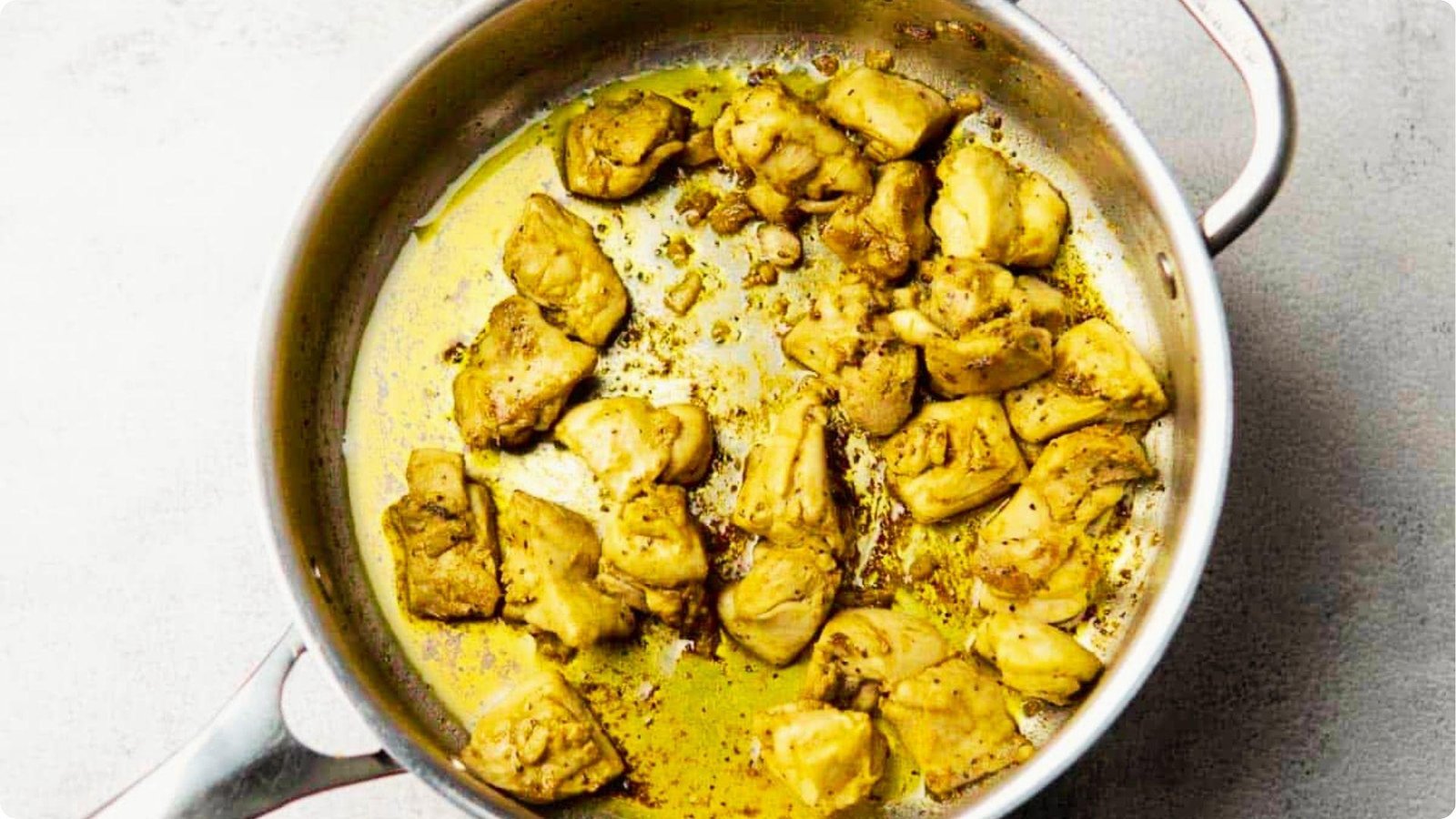 Golden-brown seasoned chicken pieces sizzling in oil in a stainless steel pan.