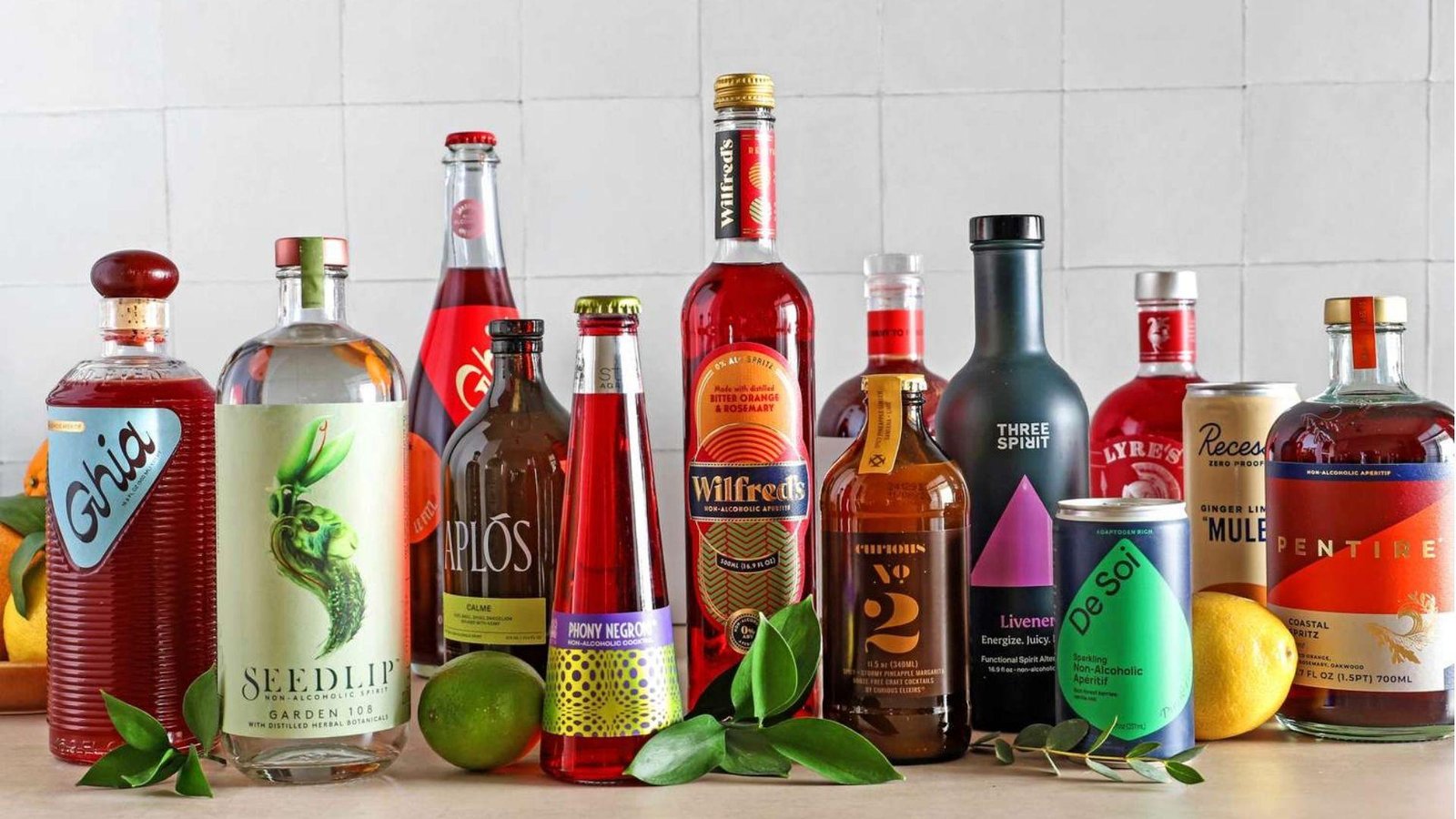 A lineup of non-alcoholic spirit bottles including Seedlip, Ghia, Aplos, Wilfred's, Three Spirit, De Soi, and Pentire on a white surface.