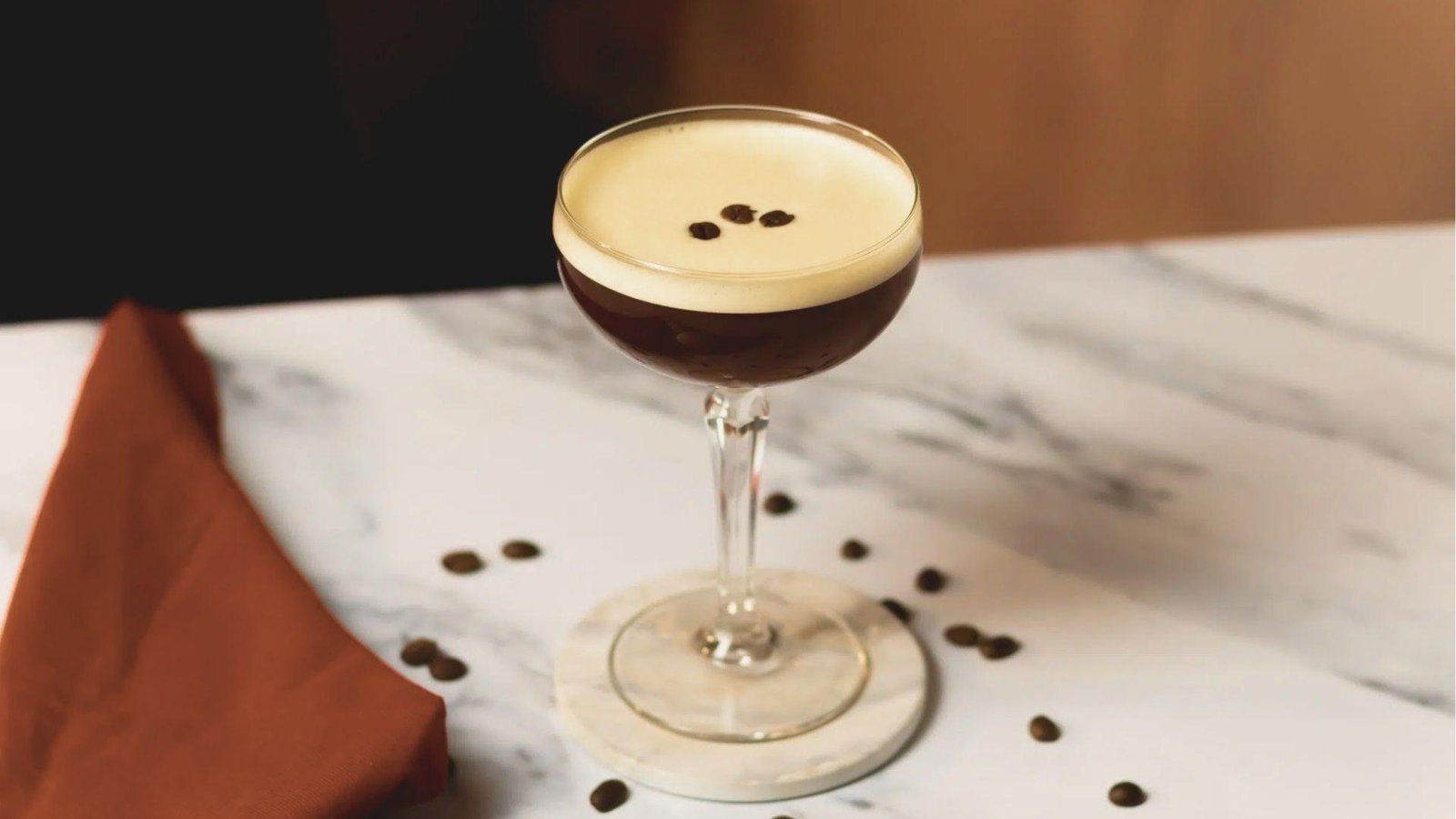 Mezcal Espresso Martini in a coupe glass with perfect foam and three-bean garnish, set on a marble counter.