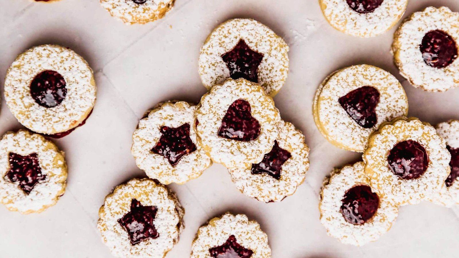 Overhead view of heart and star cutout Linzer cookies with jam filling dusted with powdered sugar