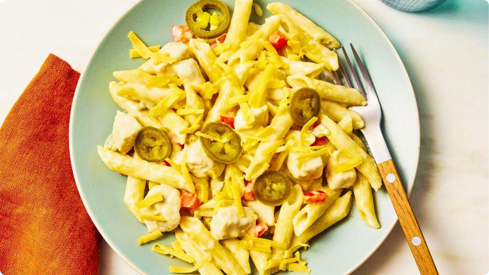 Rattlesnake pasta served on a light blue plate with penne, diced chicken, shredded cheese, and sliced jalapeños.