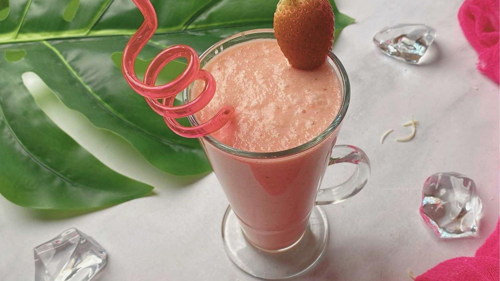 Single glass mug of creamy pink Bahama Mama Tropical Smoothie with a curly red straw and strawberry garnish.