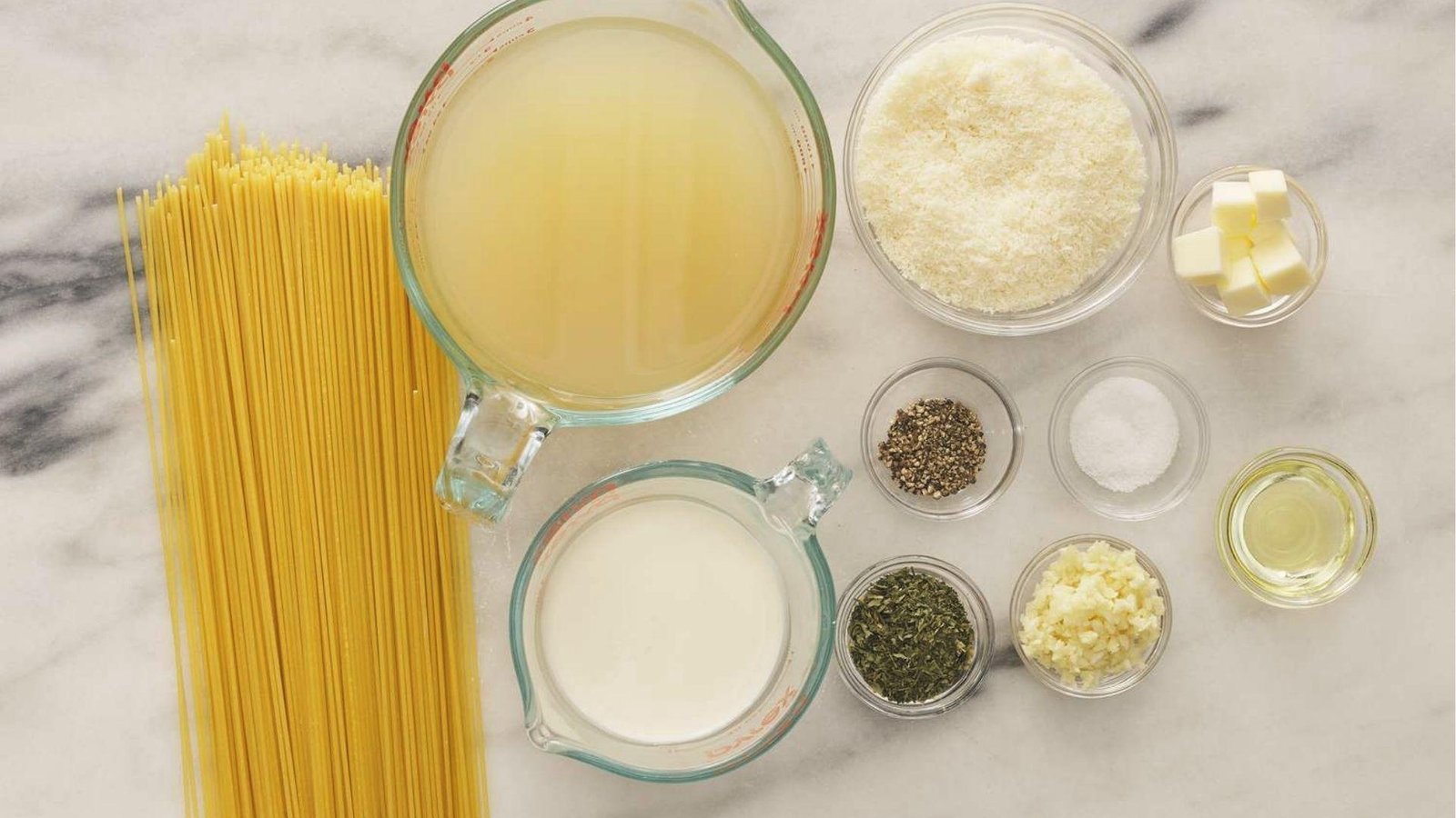 Raw spaghetti, cream, broth, cheese, butter, garlic, herbs, spices laid out for pasta recipe