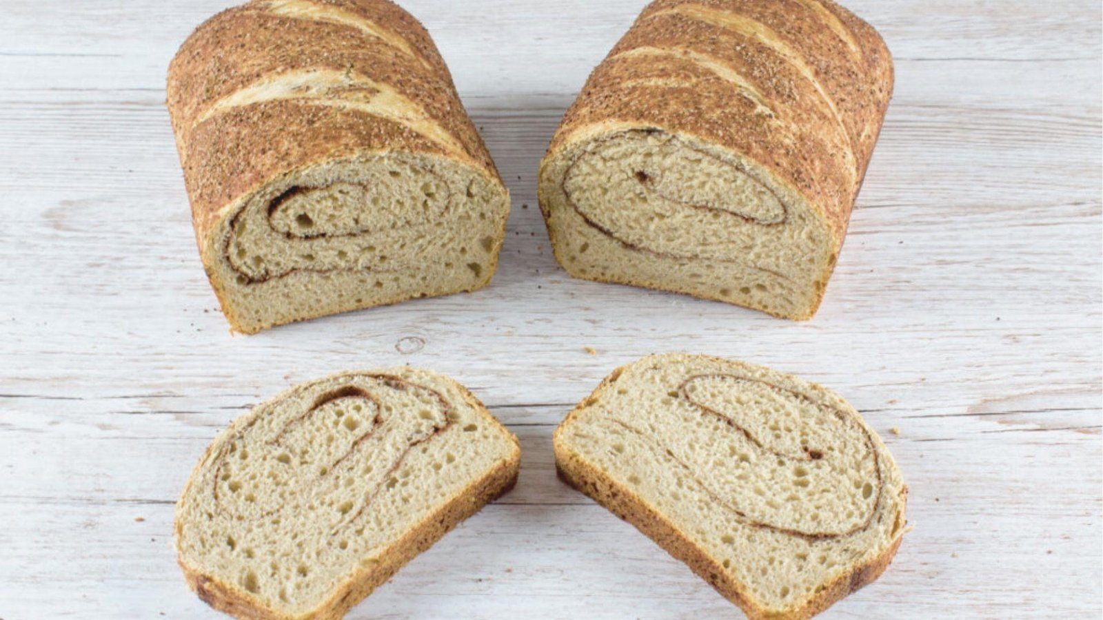 Two loaves of coffee swirl bread and two slices arranged on a white wood surface.