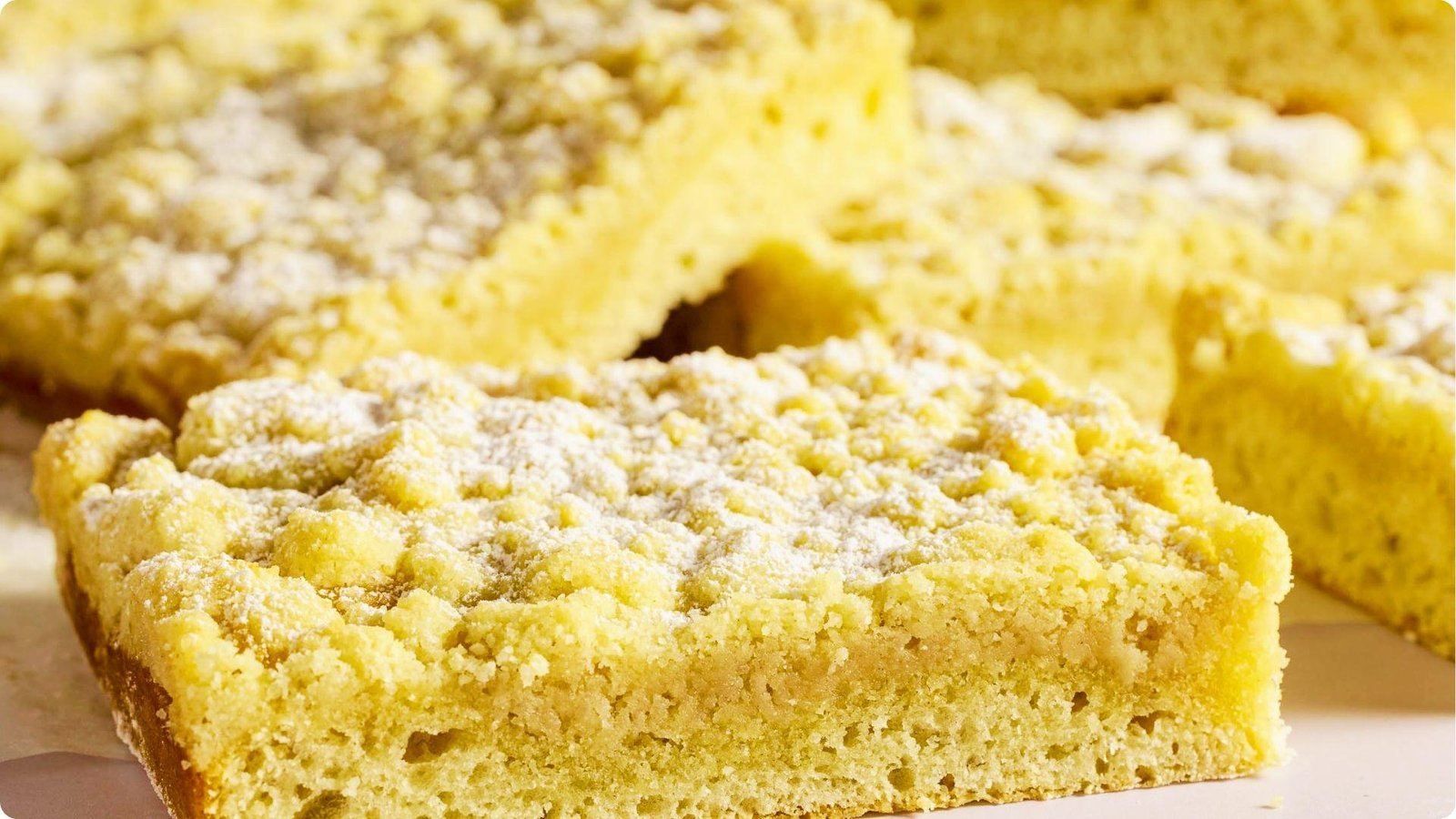 Close-up of freshly baked German coffee cake squares with a thick, crumbly streusel topping dusted with powdered sugar.