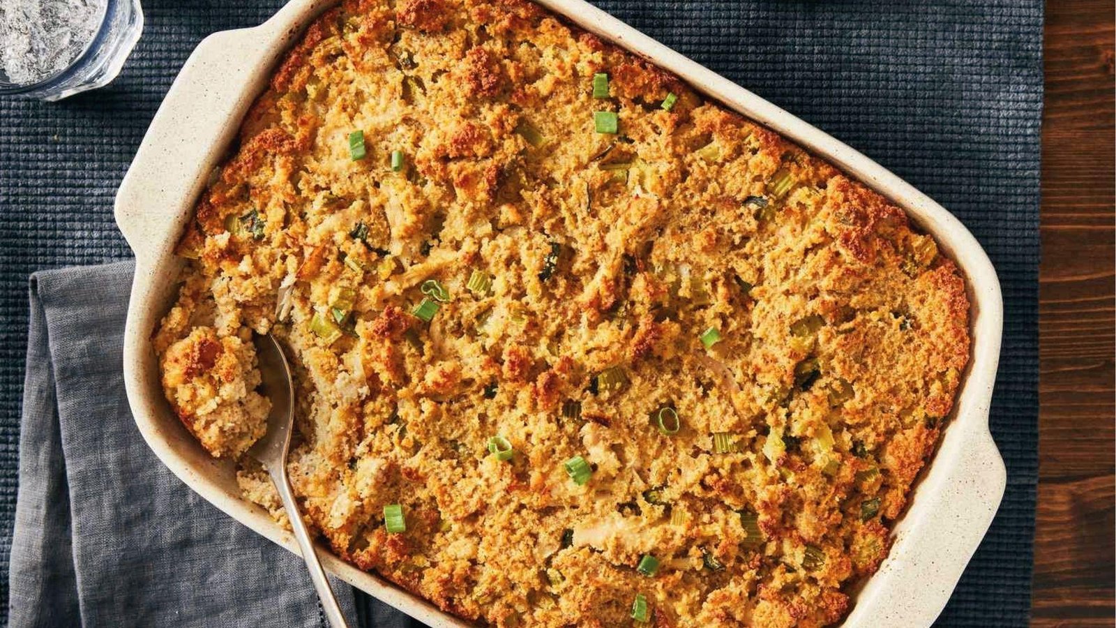 Golden baked cornbread dressing in ceramic dish topped with green onions and served with spoon
