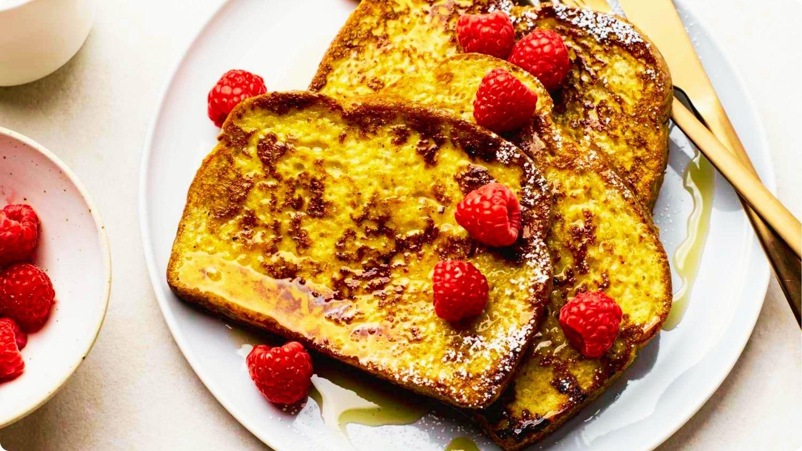 Three slices of golden wheat bread French toast on a white plate, topped with fresh raspberries.