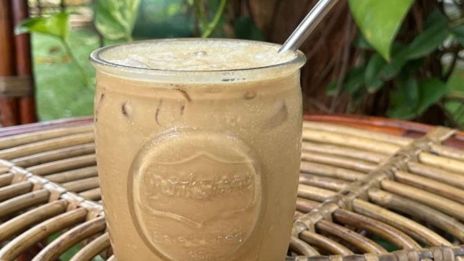 A tall iced coconut coffee drink with swirling cream and a fresh rosemary sprig garnish against a dark background.