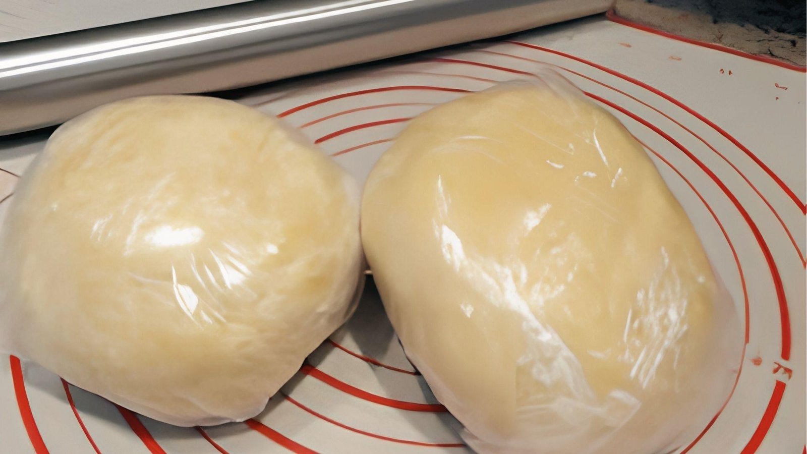 Two smooth pate sablee dough balls wrapped in plastic, chilling on silicone mat before rolling