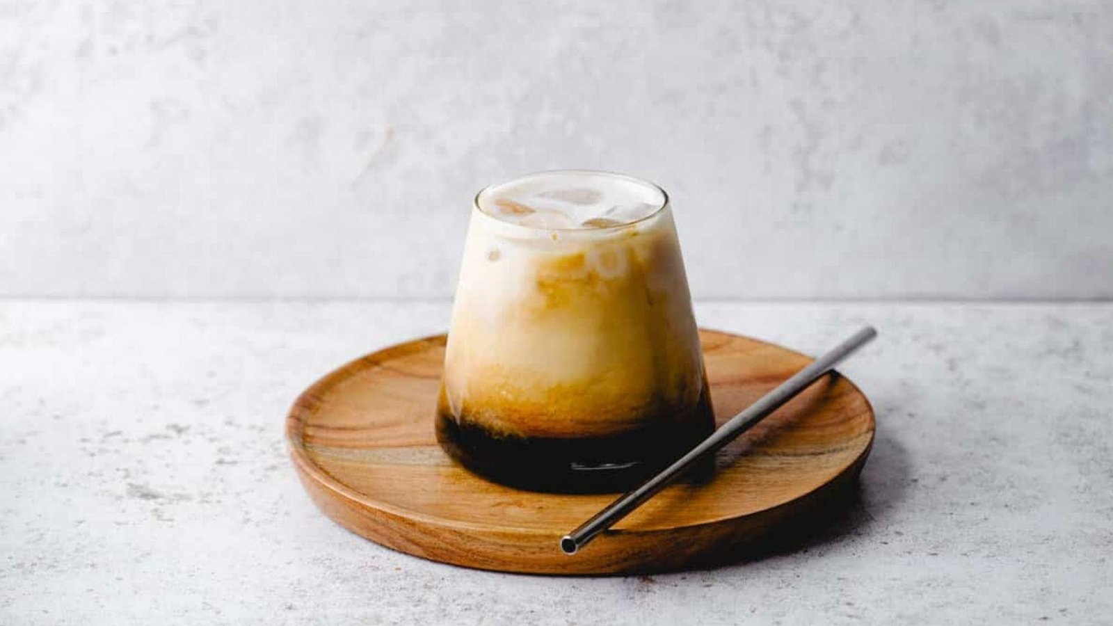 A layered iced latte in a stemless glass showing maple syrup at the bottom graduating to creamy milk on top.