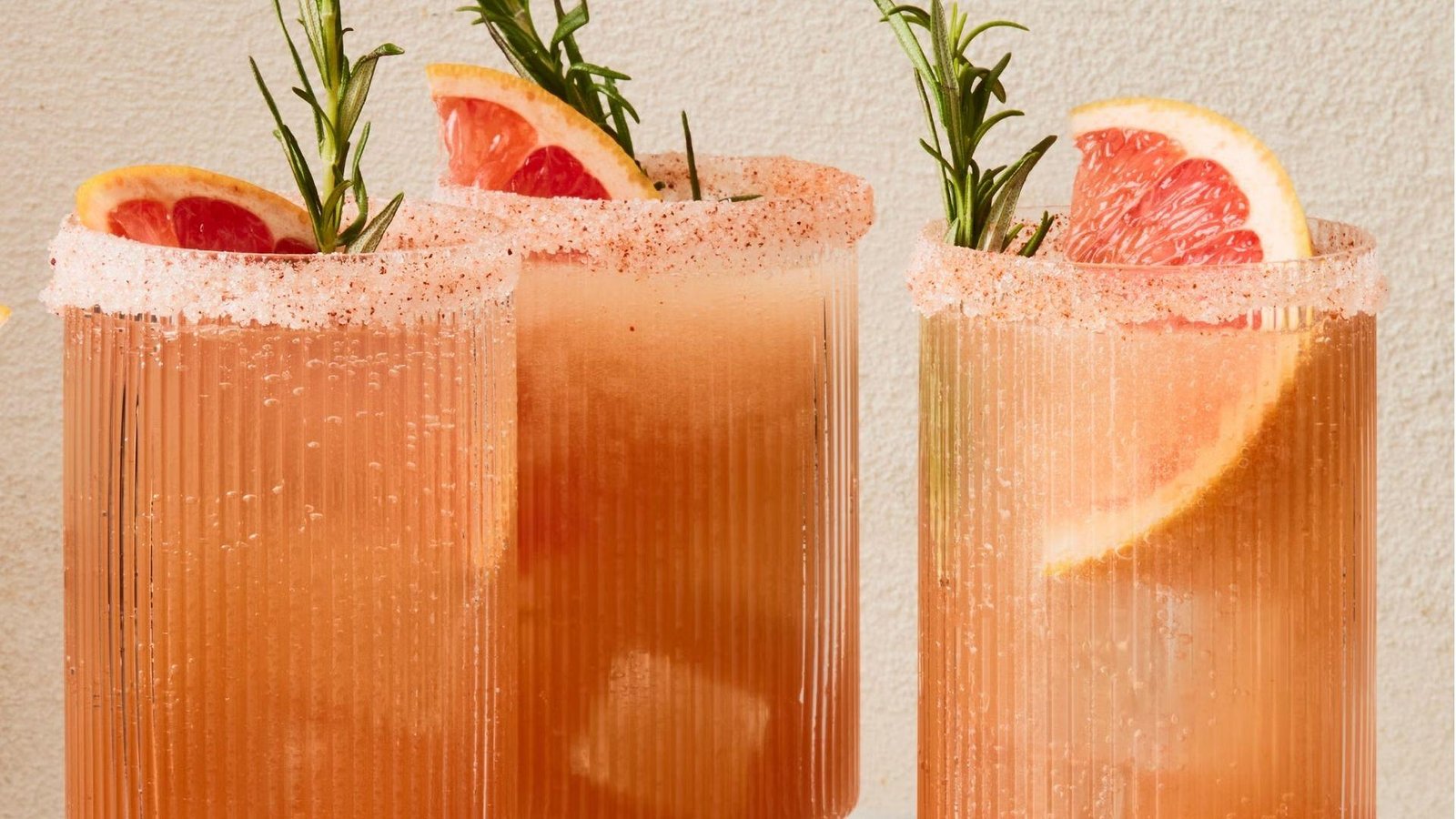 Two ribbed highball glasses of pink grapefruit mocktail with sugared rims, rosemary sprigs, and grapefruit slice garnishes.