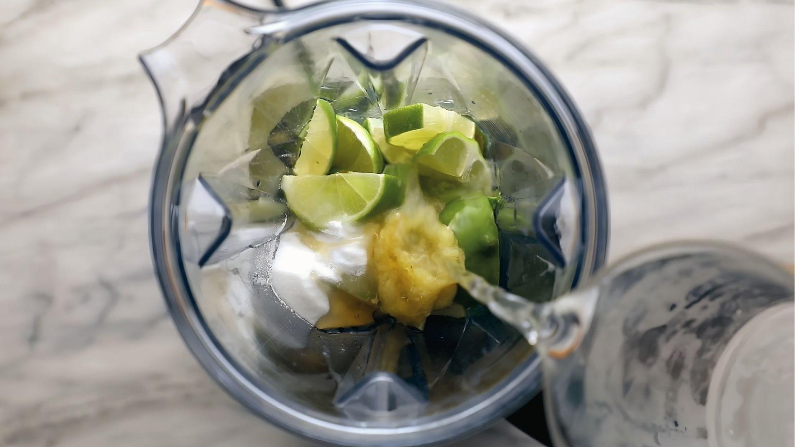 Blender filled with lime wedges, cucumber, sugar, and ice for making cucumber mint agua fresca recipe