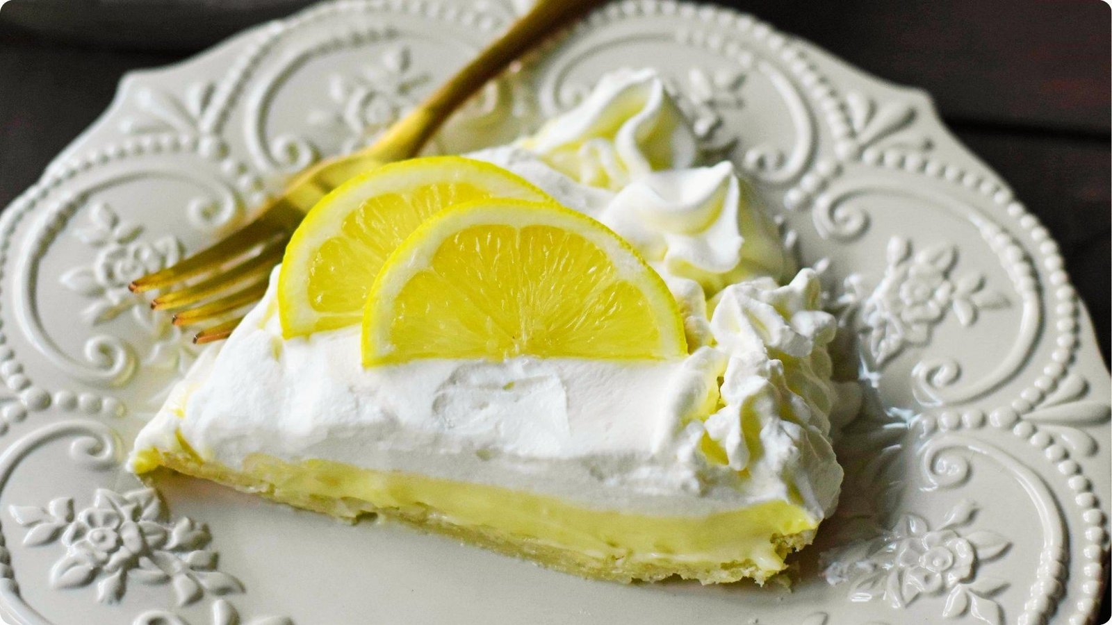 A single slice of sour cream lemon pie topped with fluffy whipped cream and fresh lemon slices.