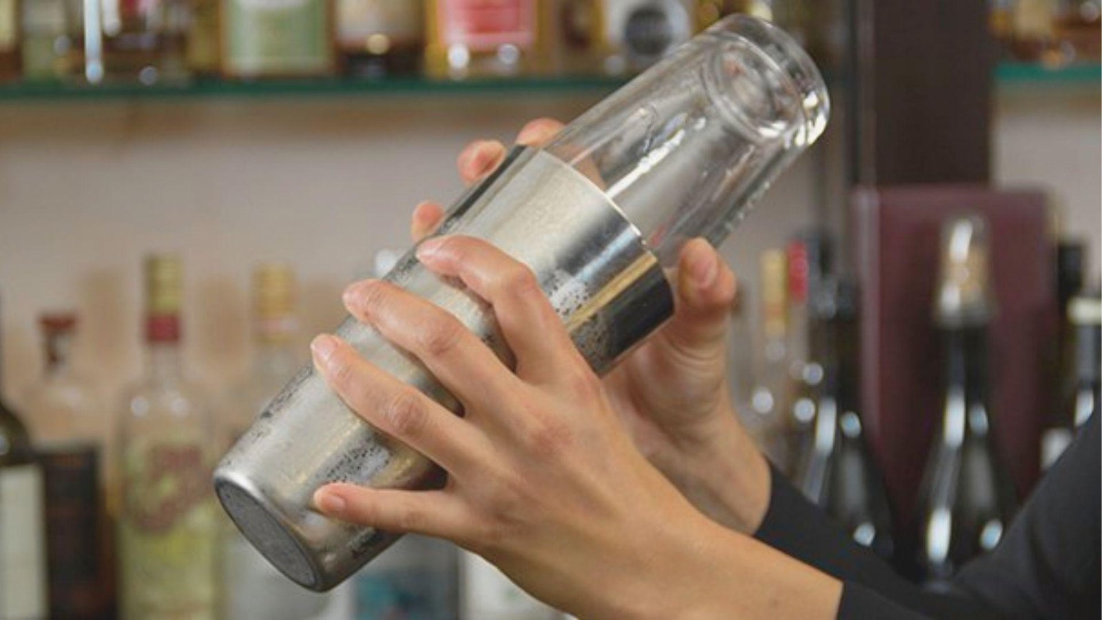 Bartender vigorously shaking a cocktail in a metal and glass Boston shaker to craft a Mezcal Espresso Martini.