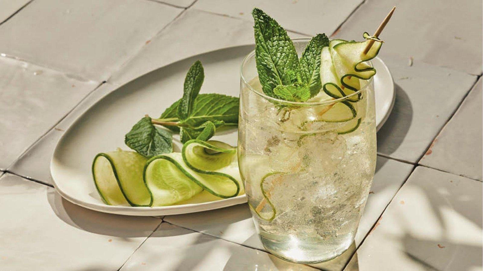 Sparkling cucumber mint agua fresca in glass with ice, garnished with mint sprig and cucumber skewer