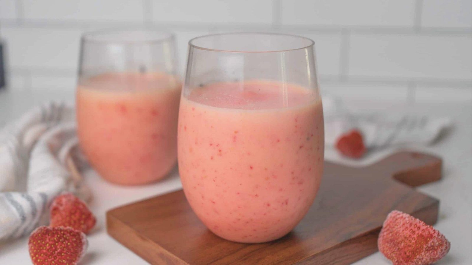 Two stemless glasses filled with light pink Bahama Mama Tropical Smoothie on a wooden board.