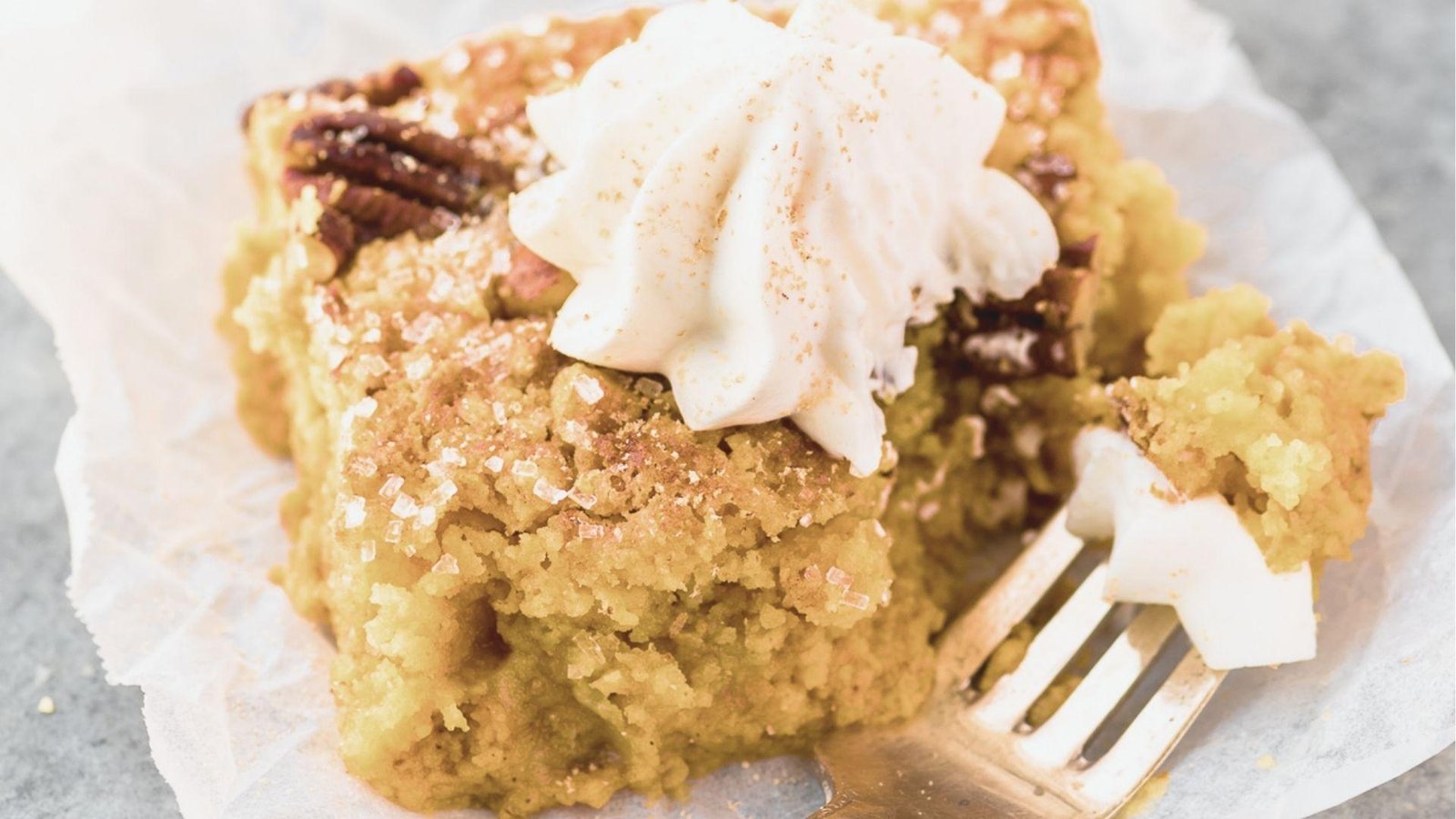 Close-up of a moist Pumpkin Crunch dessert square on parchment paper with a fork taking a bite.