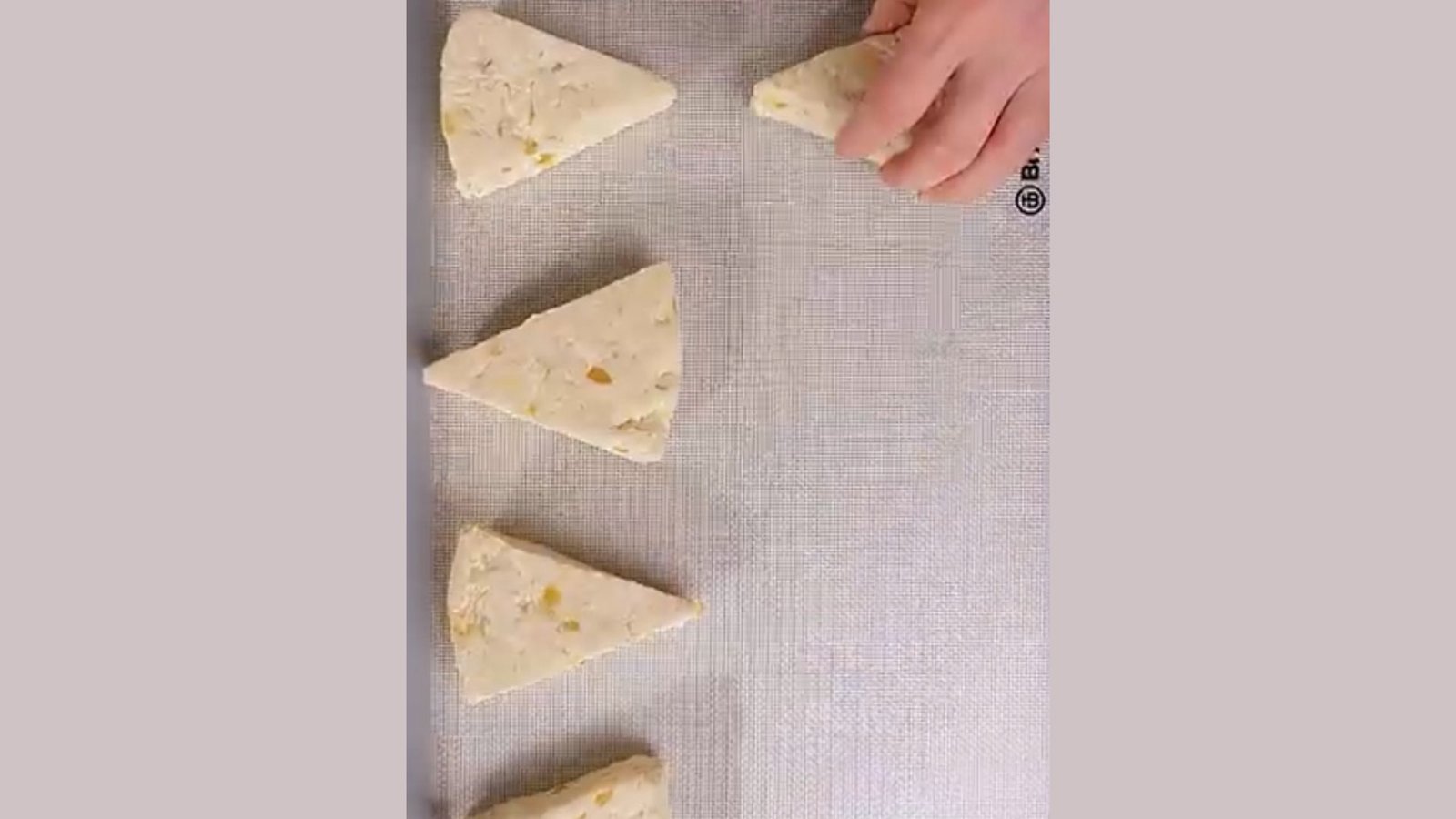 Ginger scone dough cut into wedges, brushed with cream, and sprinkled with sugar on a baking sheet.