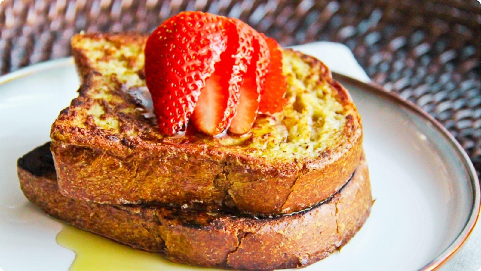 Two thick slices of wheat bread French toast stacked on a plate and drizzled with syrup.