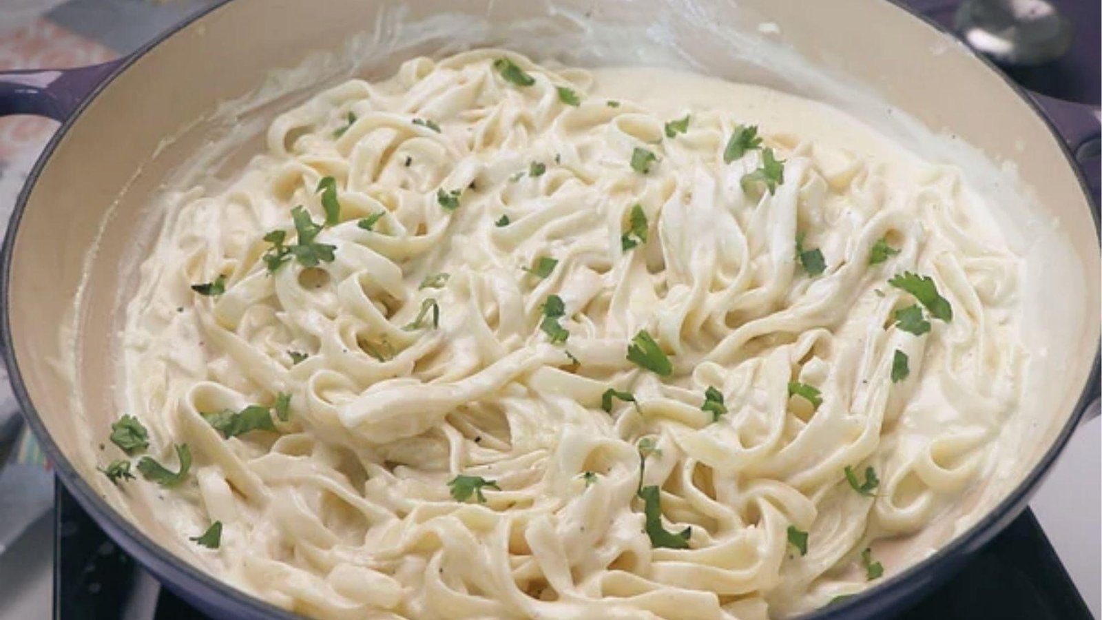Fettuccine pasta coated in thick white cream sauce garnished with fresh parsley in blue pan