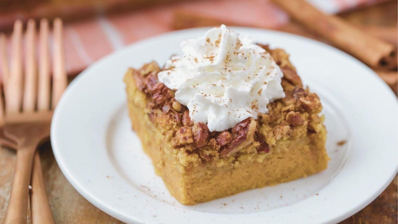 Square slice of baked Pumpkin Crunch on a white plate, topped with whipped cream and toasted pecans.