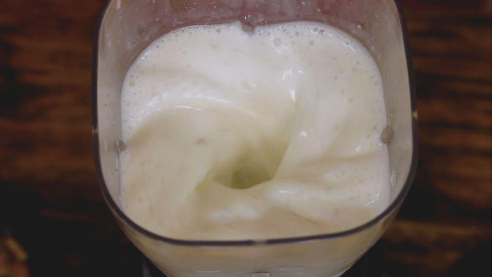 Top-down view of a creamy white coconut blend swirling in a blender pitcher.