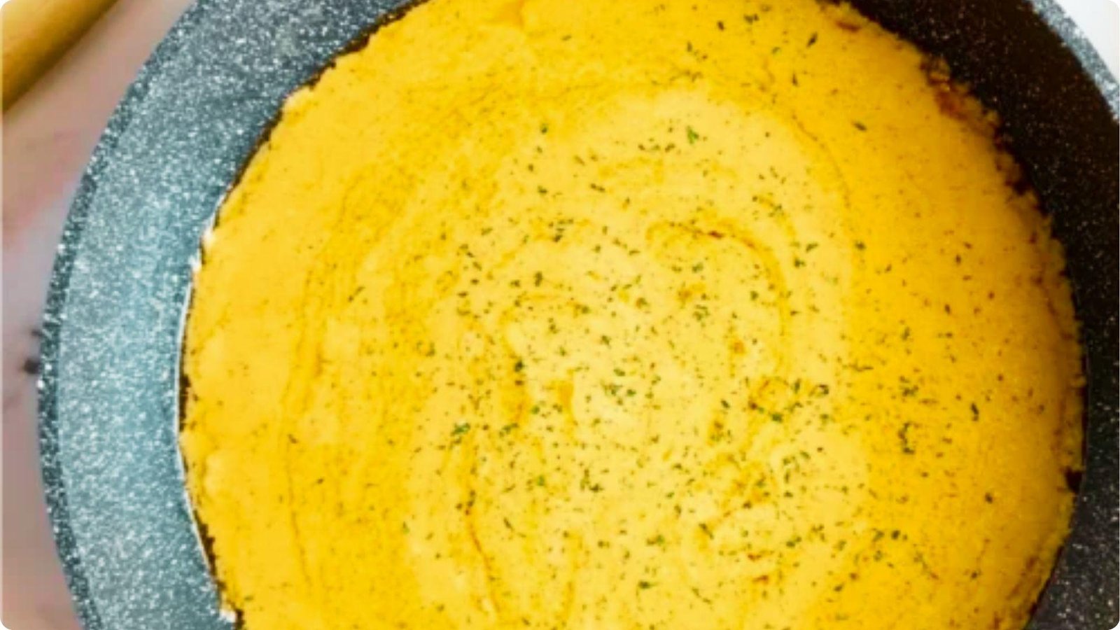 Thick, golden-yellow cheese sauce for rattlesnake pasta simmering in a speckled nonstick pan.