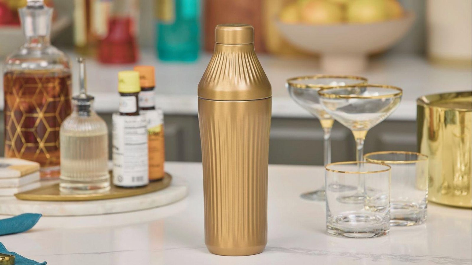 Classy gold cocktail shaker centered among bitters, decanters, and gold-rimmed coupe glasses ready for Mezcal Espresso Martinis.