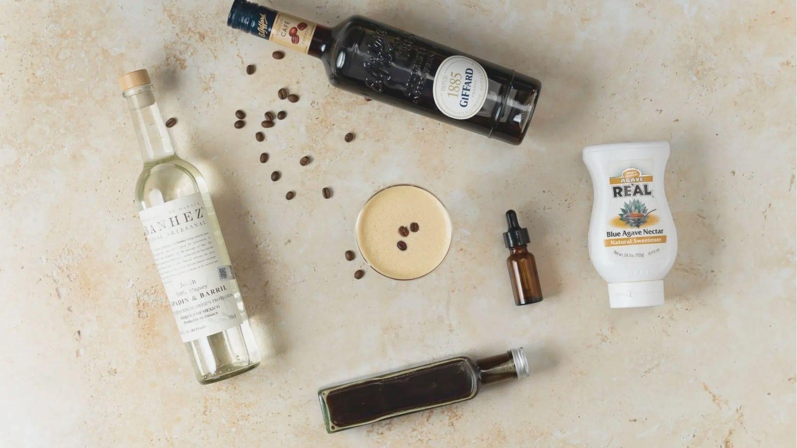 Flat lay of Mezcal Espresso Martini ingredients: Banhez mezcal, coffee liqueur, agave nectar, bitters, and scattered coffee beans.