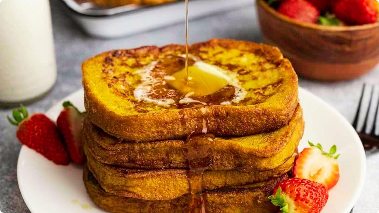 Stack of golden wheat bread French toast on a white plate topped with melting butter.