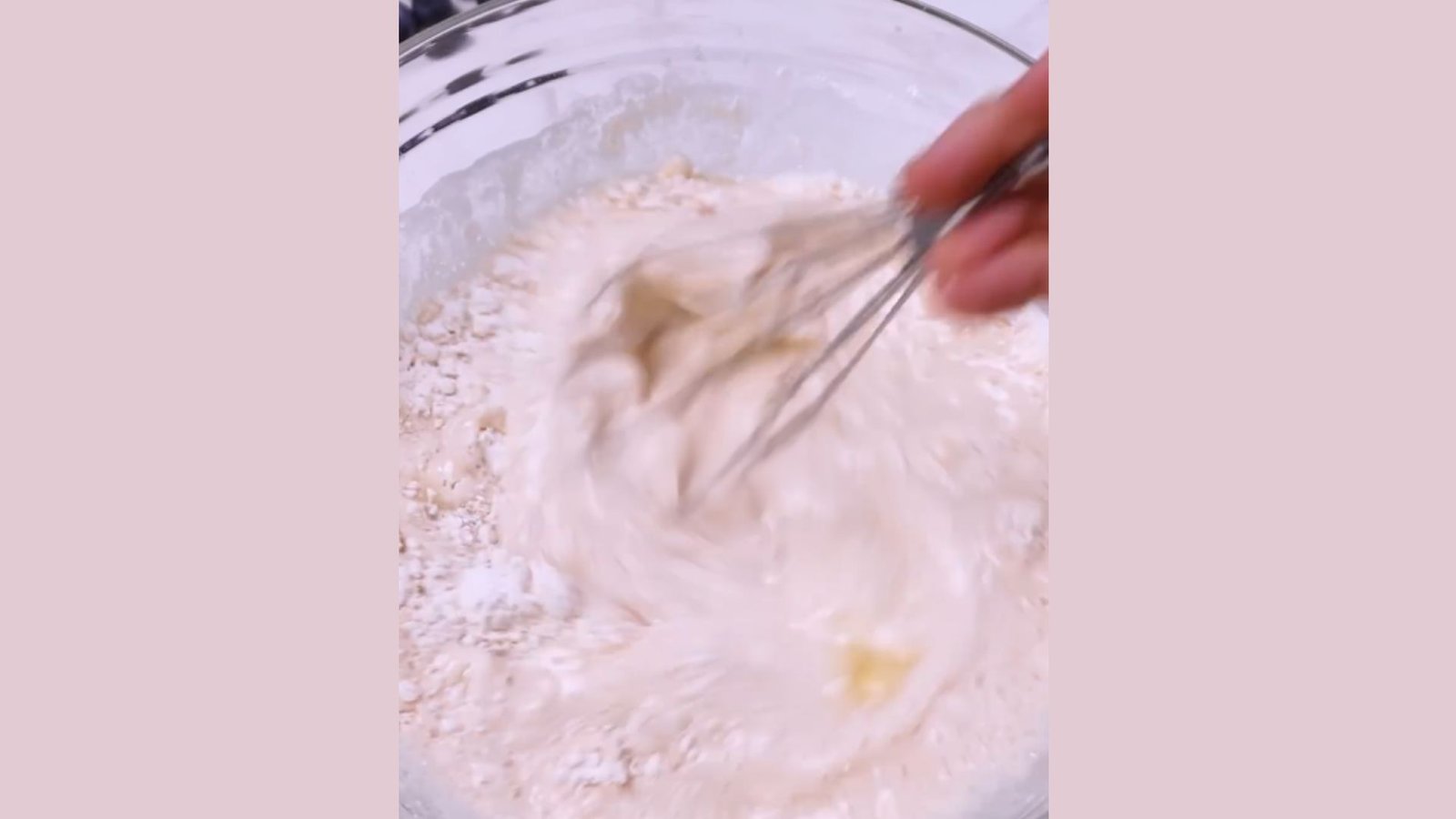 Hand whisking waffle batter mixture with visible flour lumps in clear glass bowl during mixing step