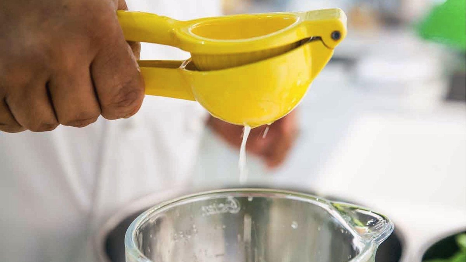 Fresh lime juice squeezed from yellow squeezer into glass pitcher for cucumber mint agua fresca base