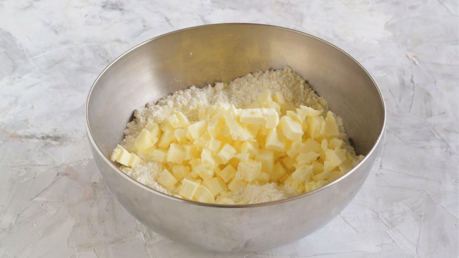 Cubed cold butter added to flour in steel bowl, first step of making pate sablee dough