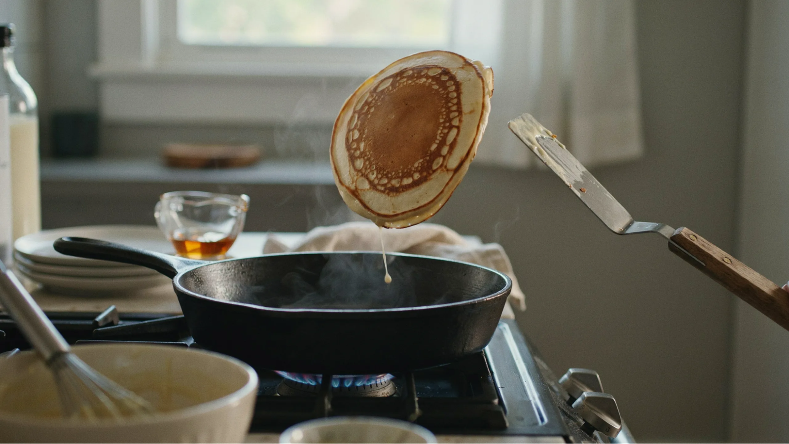 : pancake being flipped on a pan showing golden brown surface and finishing cooking evenly.
