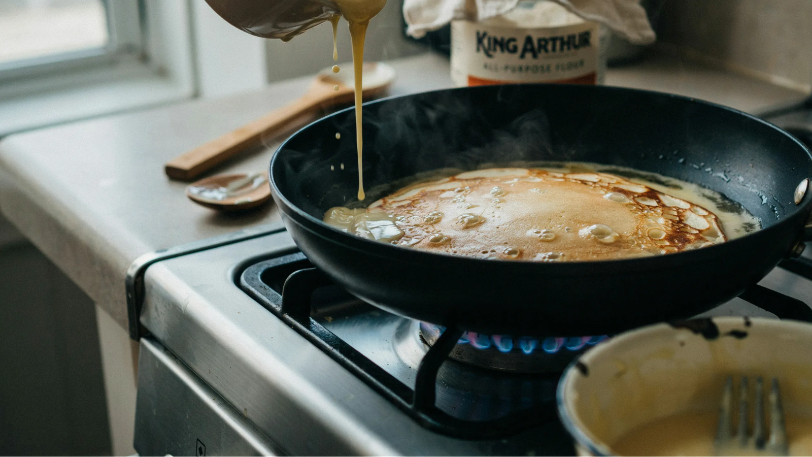  wet and dry ingredients being combined into pancake batter with slightly lumpy texture in a kitchen bowl.
